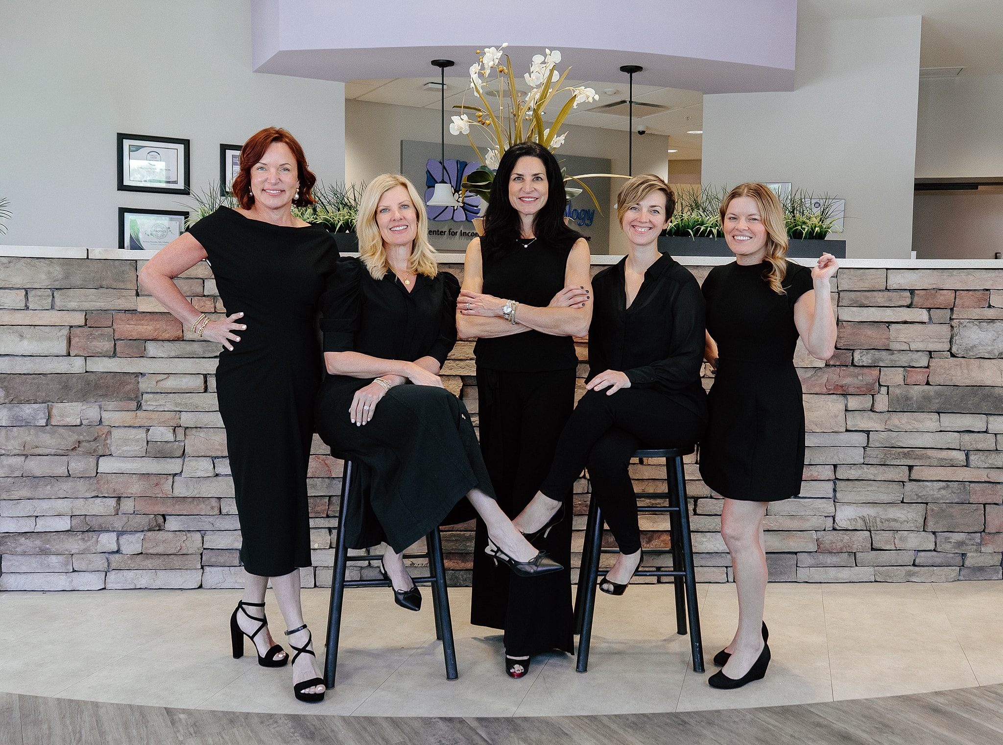 Five women in black outfits posing together.