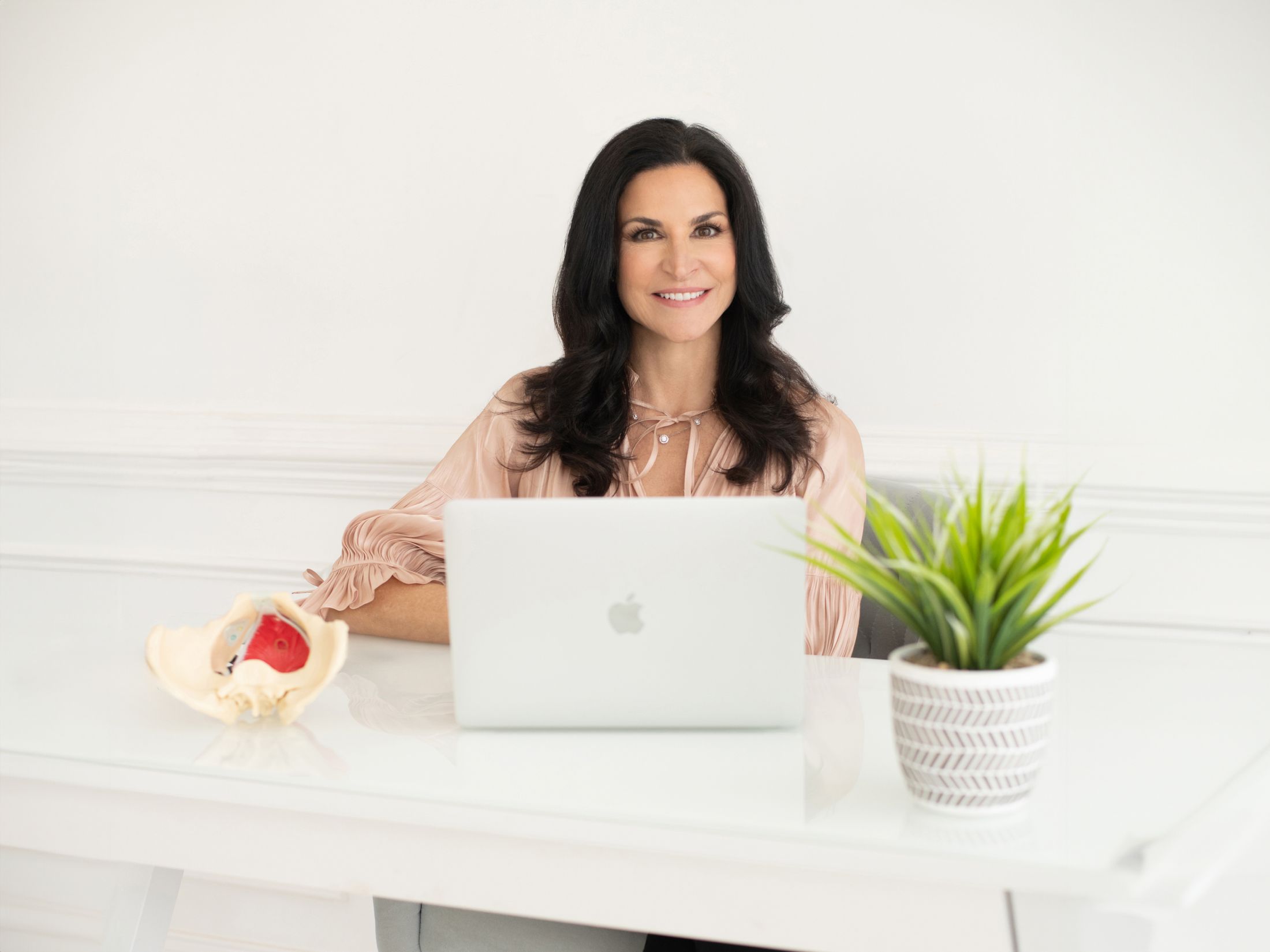 Woman at desk with laptop and anatomical model.