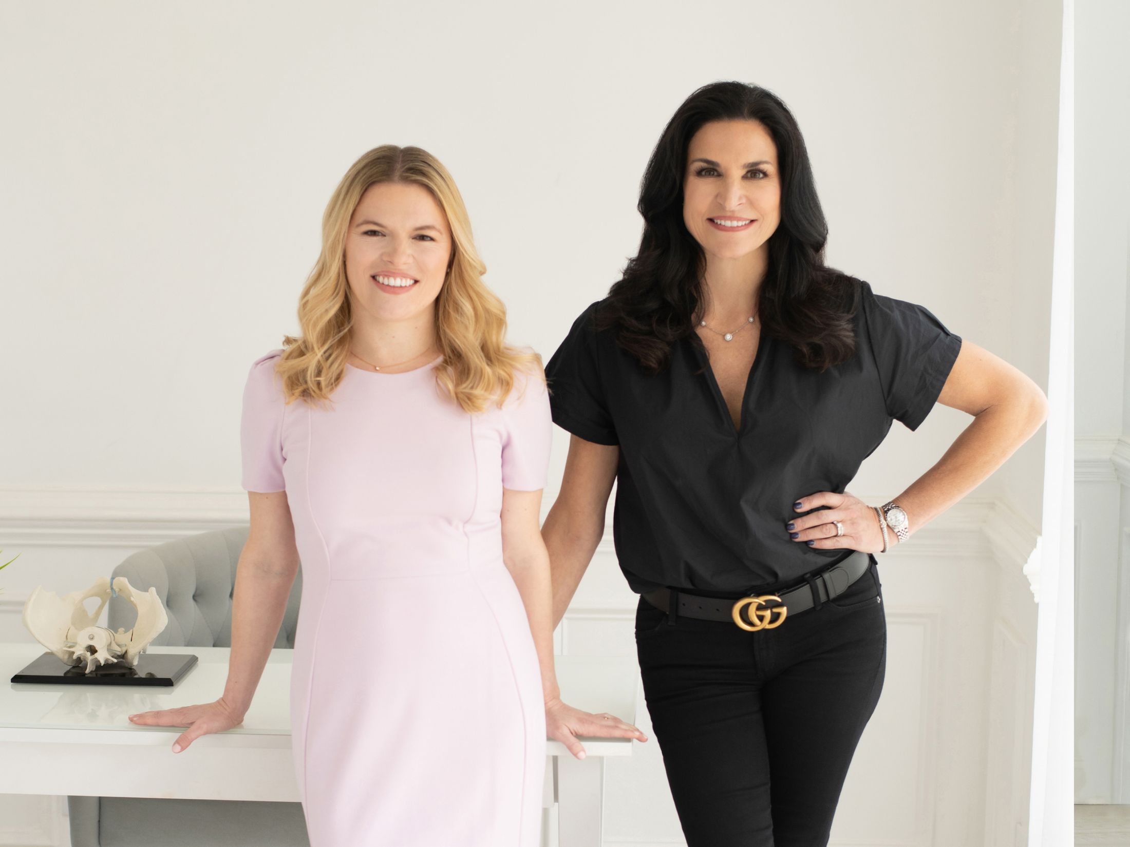 Two women posing in a modern office setting.